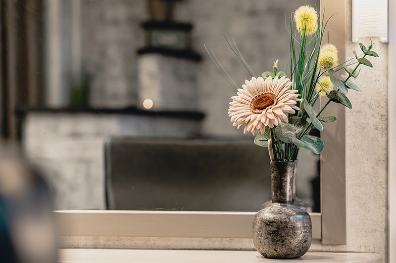 Blommor i en mörk vas på hyllan framför spegeln i salongen